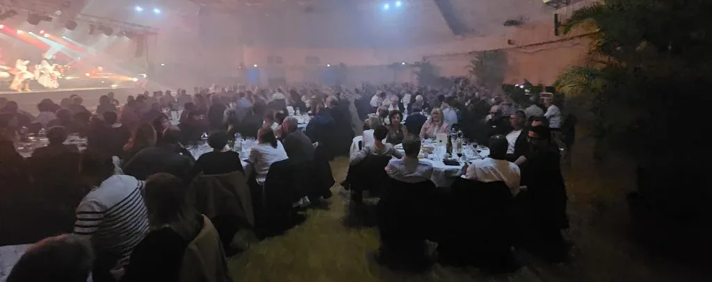 Banquet associatif : convives attablés dans une grande salle, spectacle sur scène